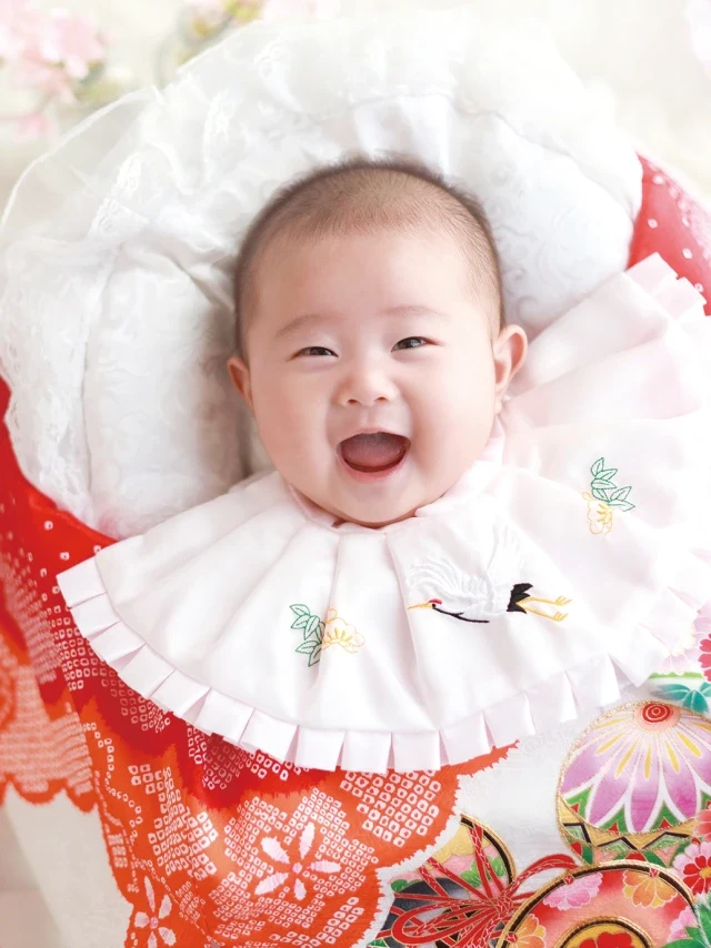 祝い着に包まれて笑うお宮参りの赤ちゃん